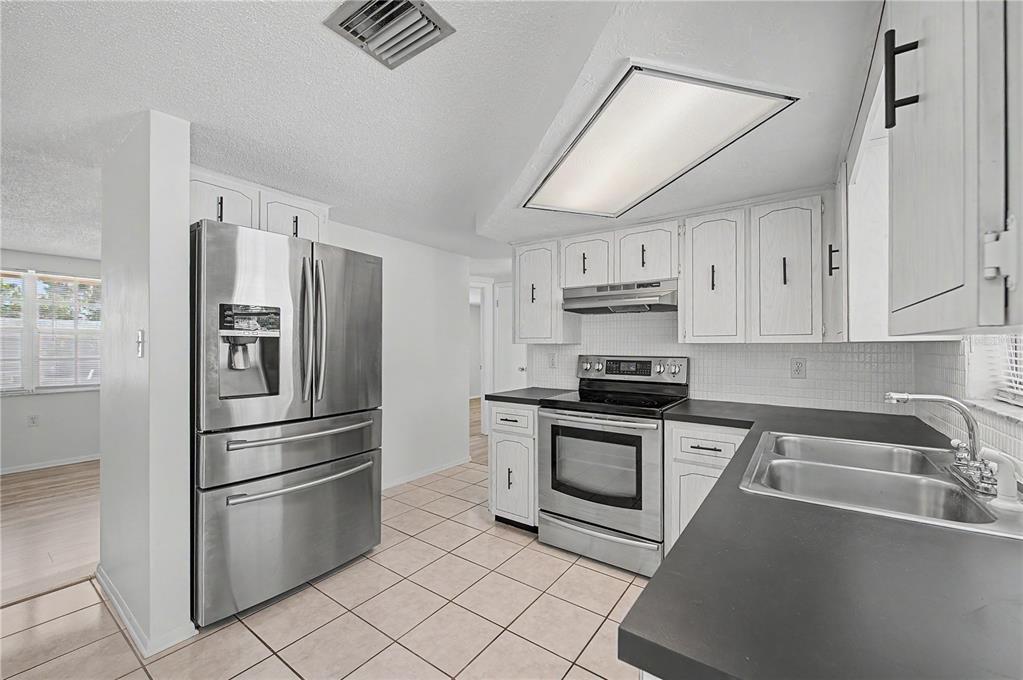 A kitchen features white cabinets, stainless steel appliances, dark countertops, and light-colored tile flooring — 9830 RAINBOW LANE, PORT RICHEY, FL