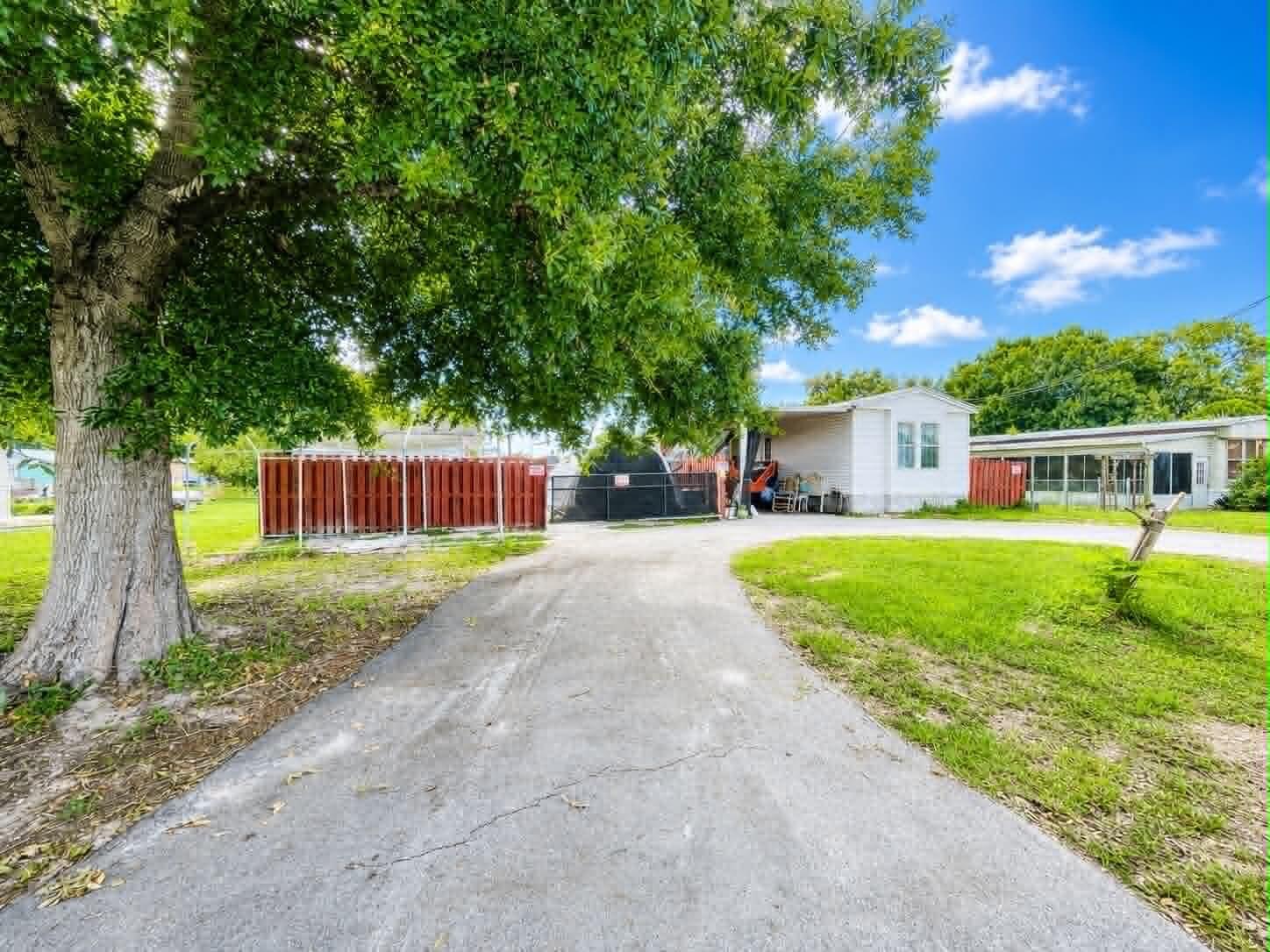 A paved driveway leads toward a white mobile home with a large tree in front — 2908 SE 37th Avenue, Okeechobee FL 34974, OKEECHOBEE, FL