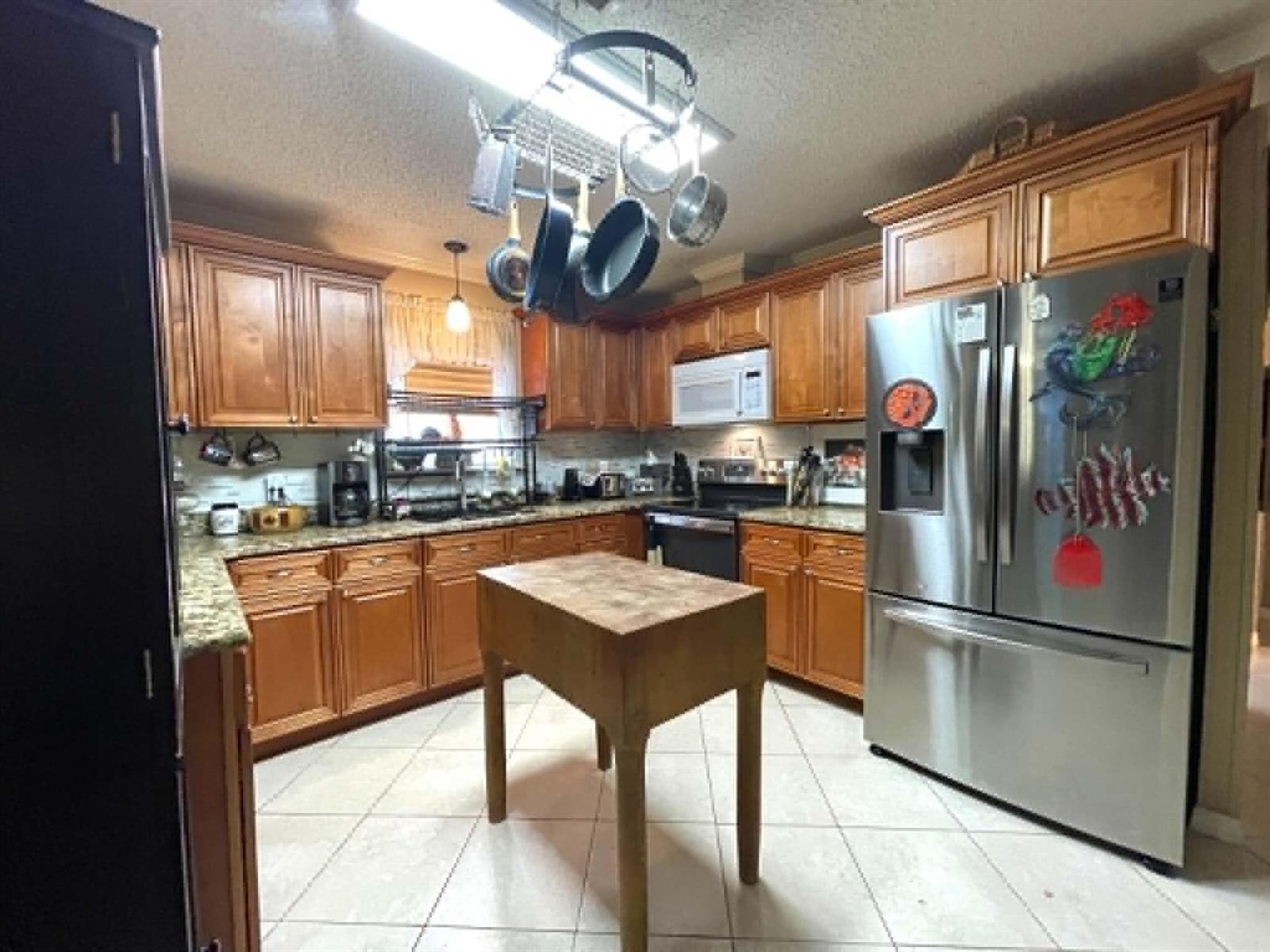 A kitchen features wood cabinets, granite countertops, a stainless steel refrigerator, and a hanging pot rack — 2908 SE 37th Avenue, Okeechobee FL 34974, OKEECHOBEE, FL