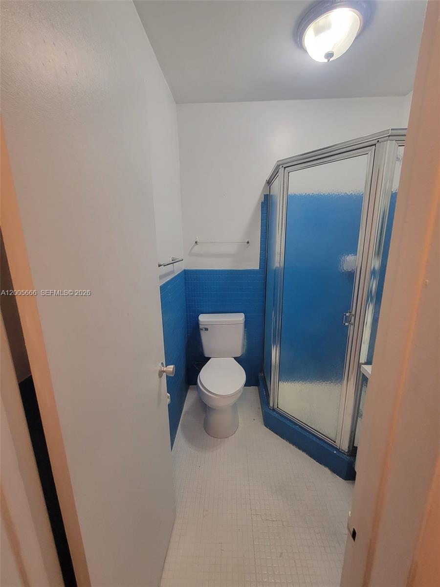 A small bathroom features a toilet, a corner shower stall, and blue tiled walls — 1490 NW 43rd Ave # 308, Lauderhill FL 33313, LAUDERHILL, FL