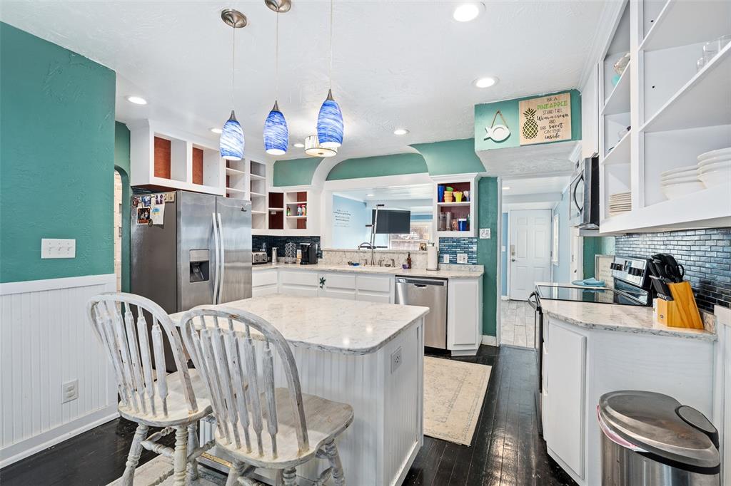 A kitchen features teal walls, white cabinets, a marble-topped island, and dark wood flooring — 129 S WILD OLIVE AVENUE, DAYTONA BEACH, FL