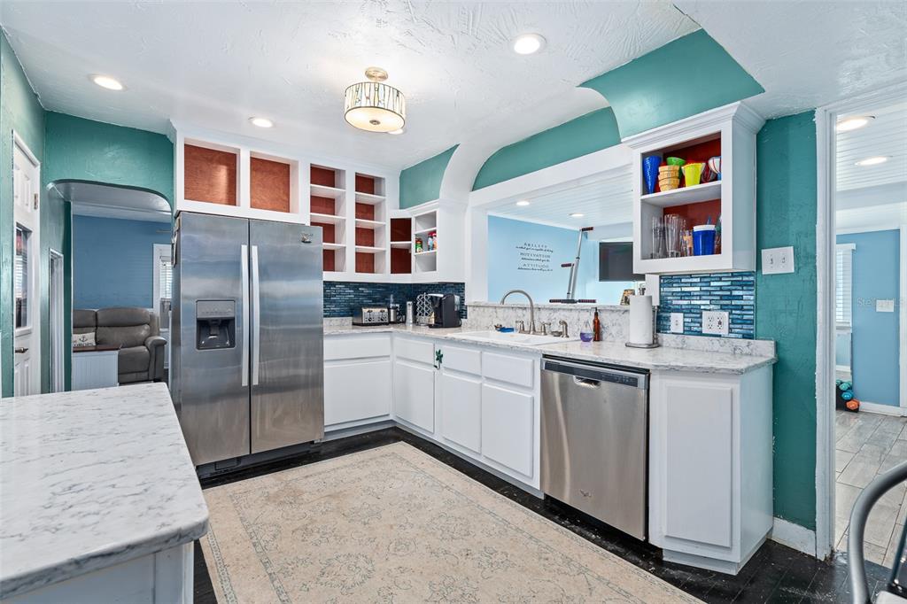 A kitchen features white cabinets, stainless steel appliances, teal walls, and a marble-patterned countertop — 129 S WILD OLIVE AVENUE, DAYTONA BEACH, FL