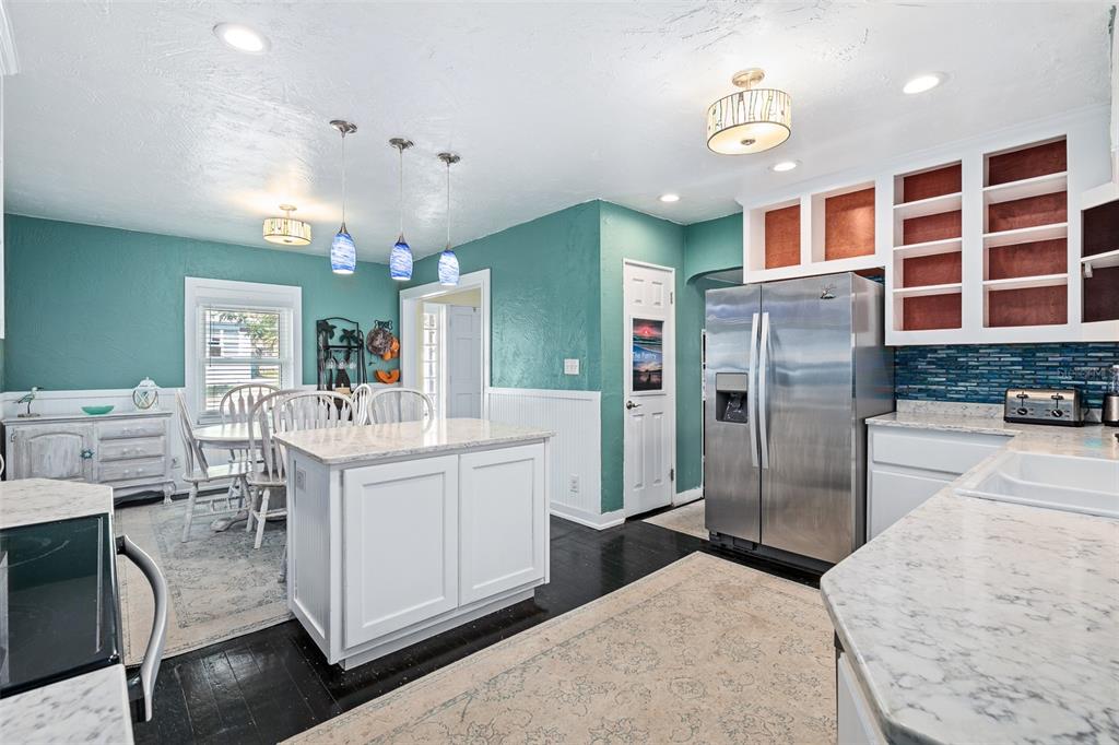 A kitchen features teal walls, white cabinetry, a marble-topped island, and dark wood flooring — 129 S WILD OLIVE AVENUE, DAYTONA BEACH, FL