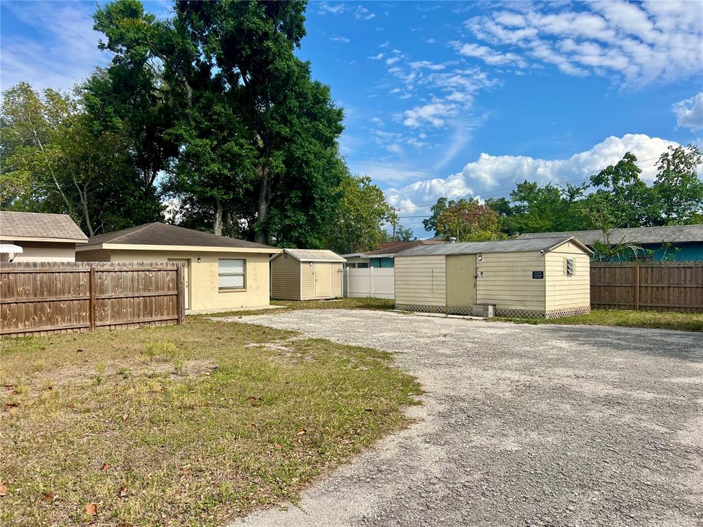 A gravel lot features two small storage sheds and a wooden fence under a blue sky — 3110 W IVY STREET, TAMPA, FL