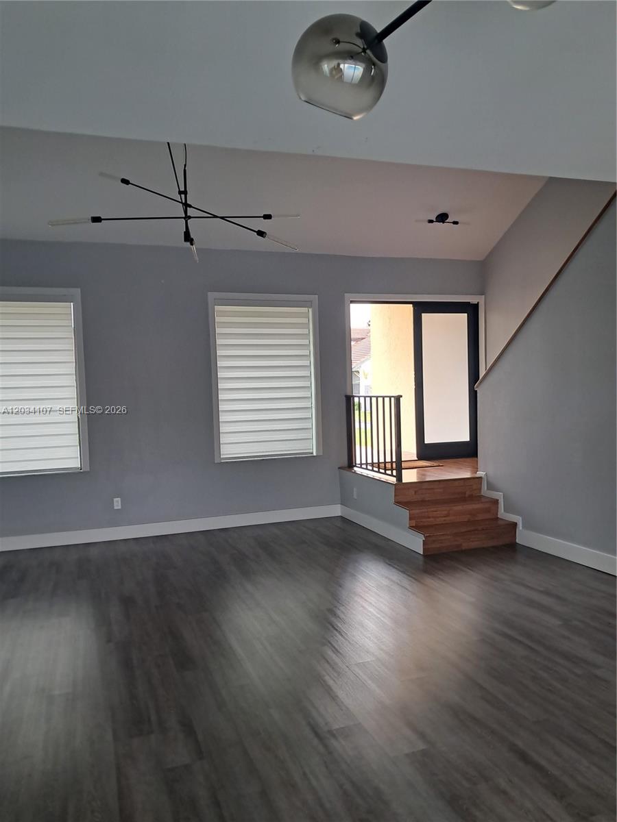 A living room features gray walls, dark wood-look flooring, a modern chandelier, and stairs — MIAMI, FL