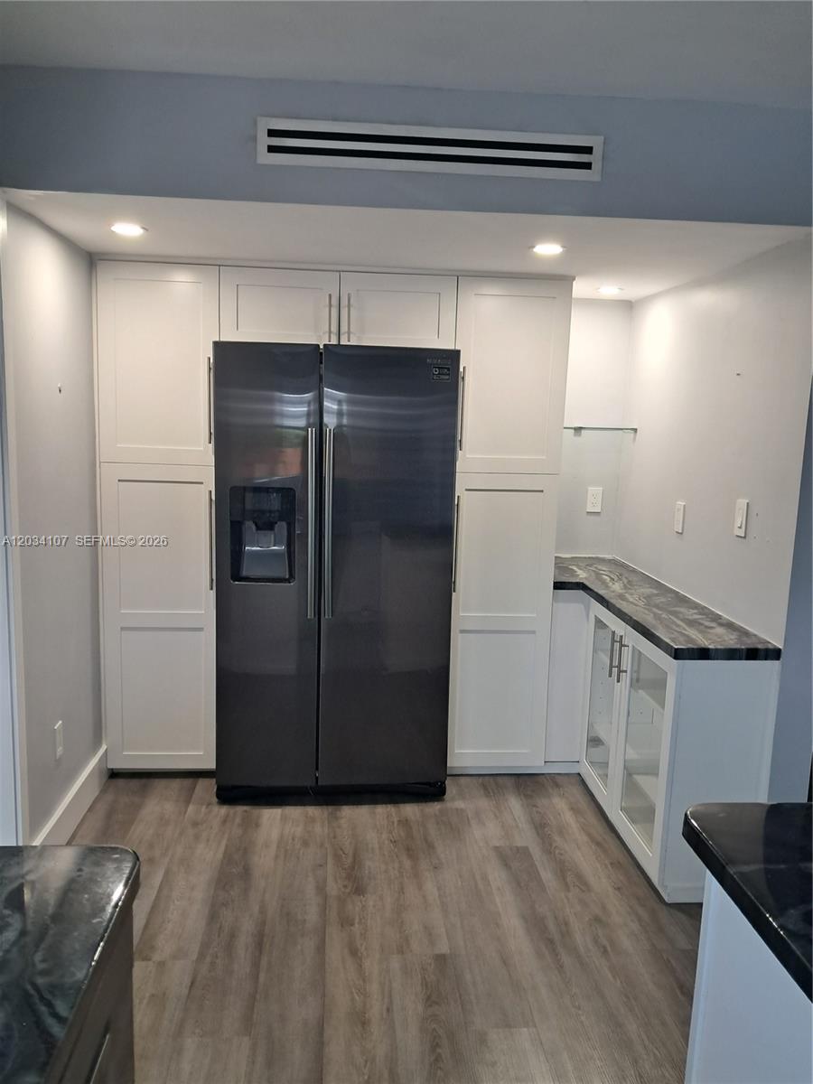 A kitchen features white cabinetry, a dark stainless steel refrigerator, and black stone countertops — MIAMI, FL