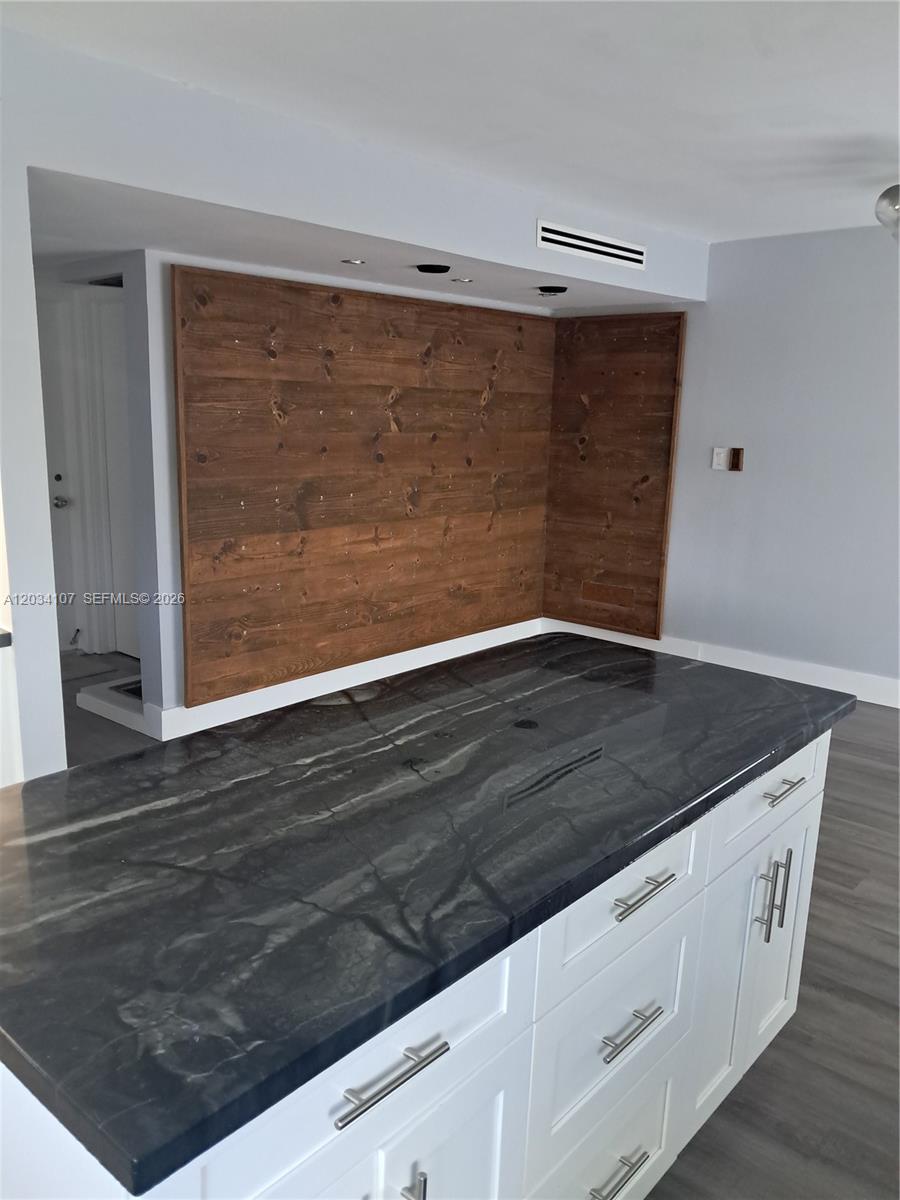A kitchen island with a dark stone countertop sits before a wood-paneled accent wall — MIAMI, FL
