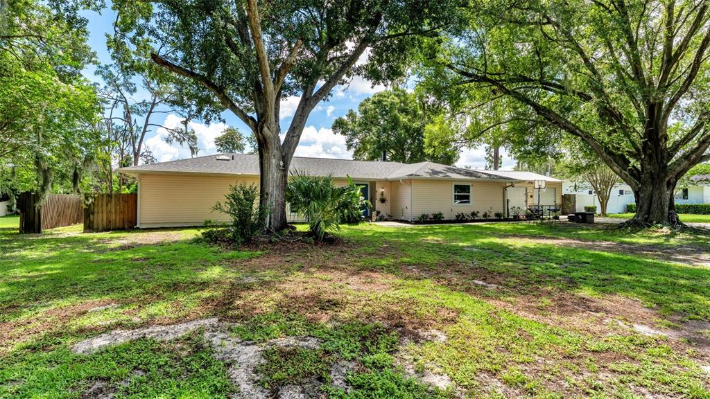 A single-story house with light-colored siding is surrounded by large trees and a grassy yard — 6114 WENDEL WAY, LAKELAND, FL