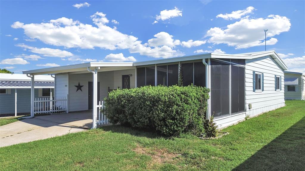 A single-story manufactured home with a carport, screened-in porch, and a large front hedge — 1802 SHERWOOD HILL DR, LAKELAND, FL