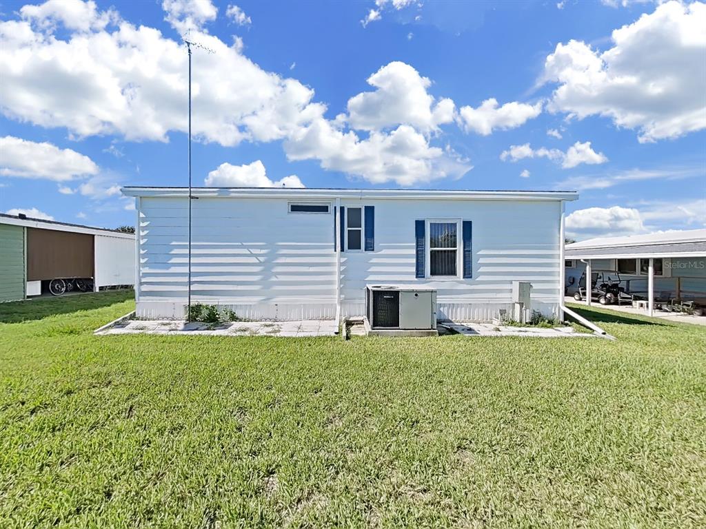 The exterior of a white mobile home features a central air conditioning unit and lawn — 1802 SHERWOOD HILL DR, LAKELAND, FL