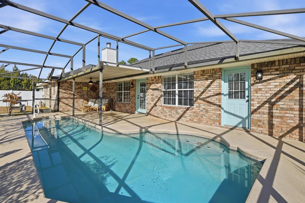 A swimming pool sits on a concrete patio enclosed by a screened-in lanai structure — 14 ROXANNE LANE, PALM COAST, FL