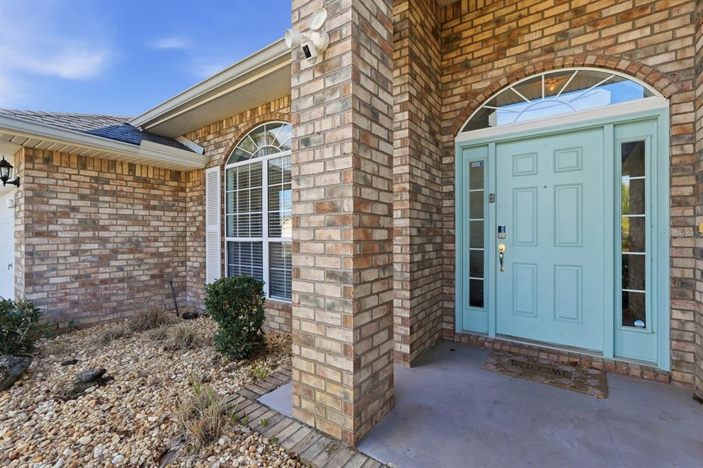 A brick house exterior features a light blue front door with sidelights and an arched transom — 14 ROXANNE LANE, PALM COAST, FL
