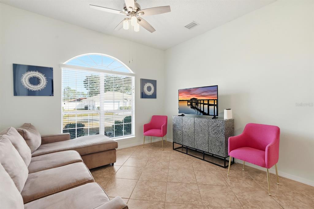 A living room features a tan sectional sofa, two pink chairs, and a television console — 14 ROXANNE LANE, PALM COAST, FL