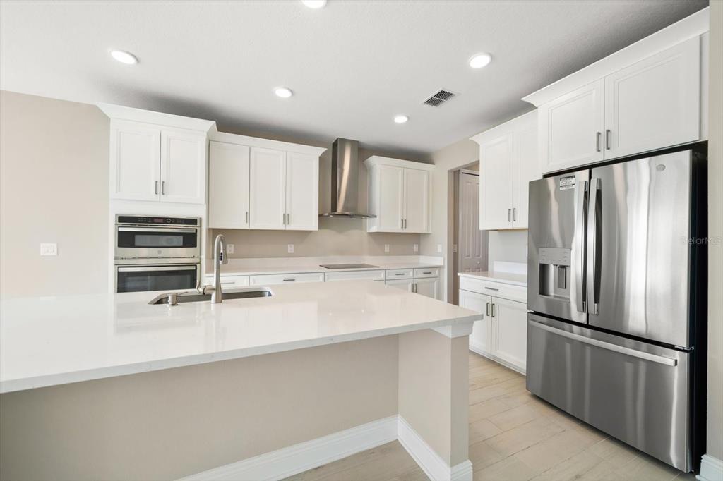 A modern kitchen features white cabinets, stainless steel appliances, and a large white quartz island — 5707 MAYDALE AVENUE, WESLEY CHAPEL, FL