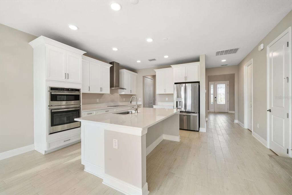 A modern kitchen features white cabinetry, stainless steel appliances, a quartz island, and light flooring — 5707 MAYDALE AVENUE, WESLEY CHAPEL, FL