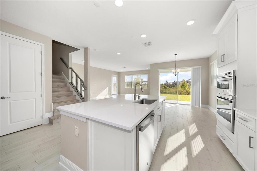 A modern kitchen with white cabinetry, a central island, and light wood-look flooring — 5707 MAYDALE AVENUE, WESLEY CHAPEL, FL