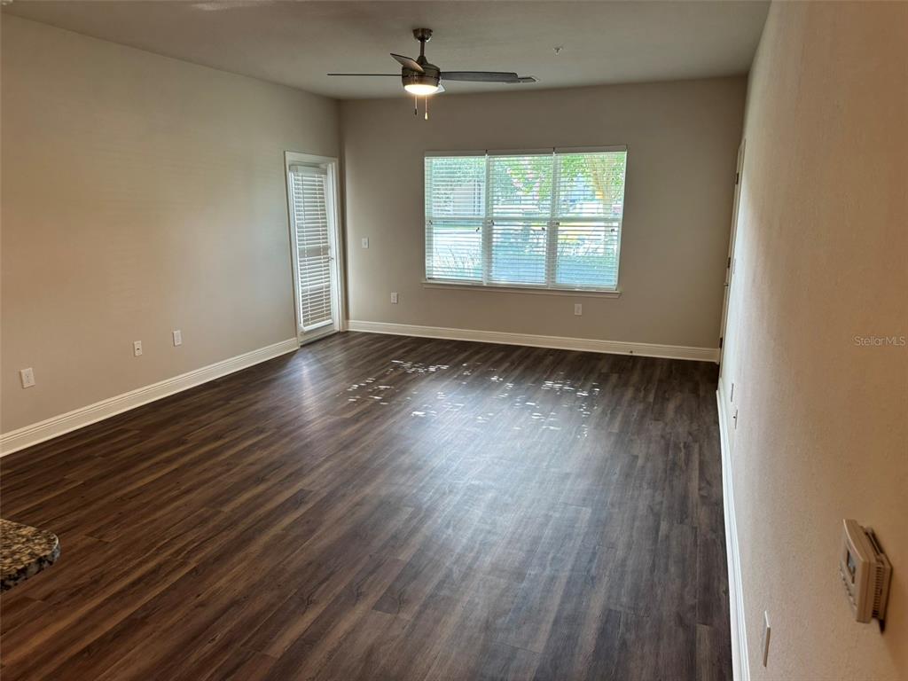 An empty living room features dark wood-look flooring, a ceiling fan, and large windows — 2460 ANN ROU ROAD UNIT 606, TAVARES, FL