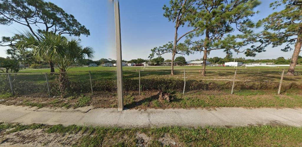 A chain-link fence separates a sidewalk from a large, grassy vacant lot with pine trees — HWY 60 E, LAKE WALES, FL