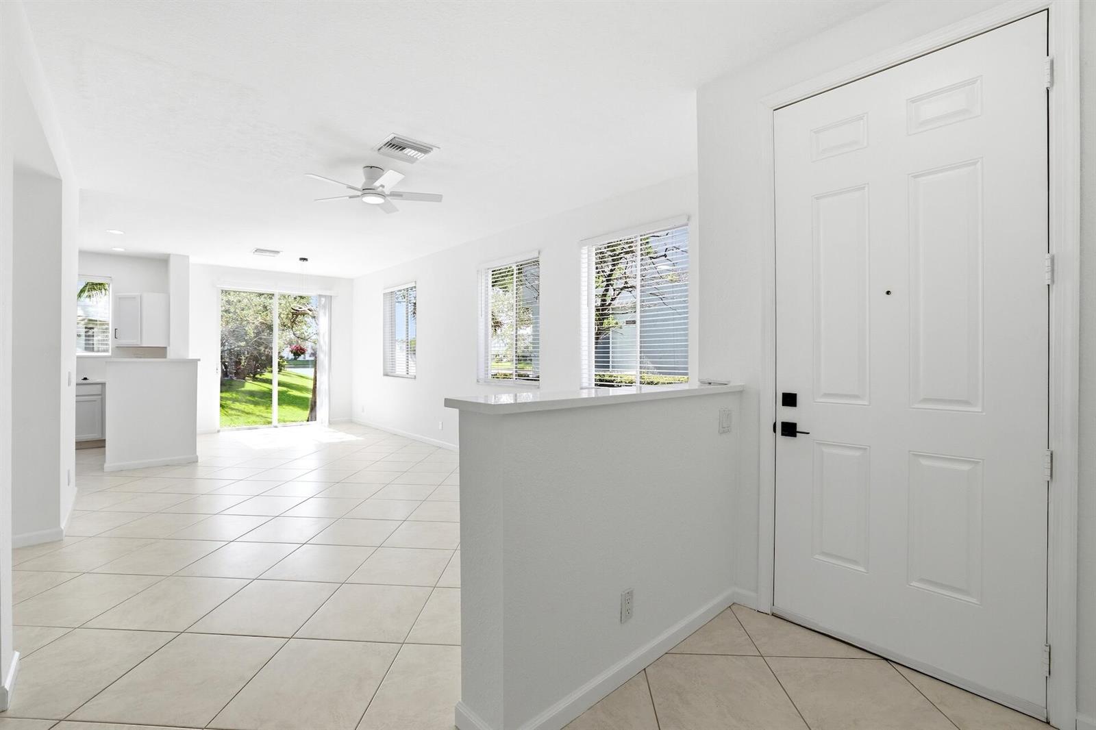 A bright, open-concept living area features white walls, tile flooring, and a front entryway door — 3068 Laurel Ridge Circle, Riviera Beach FL 33404, RIVIERA BEACH, FL