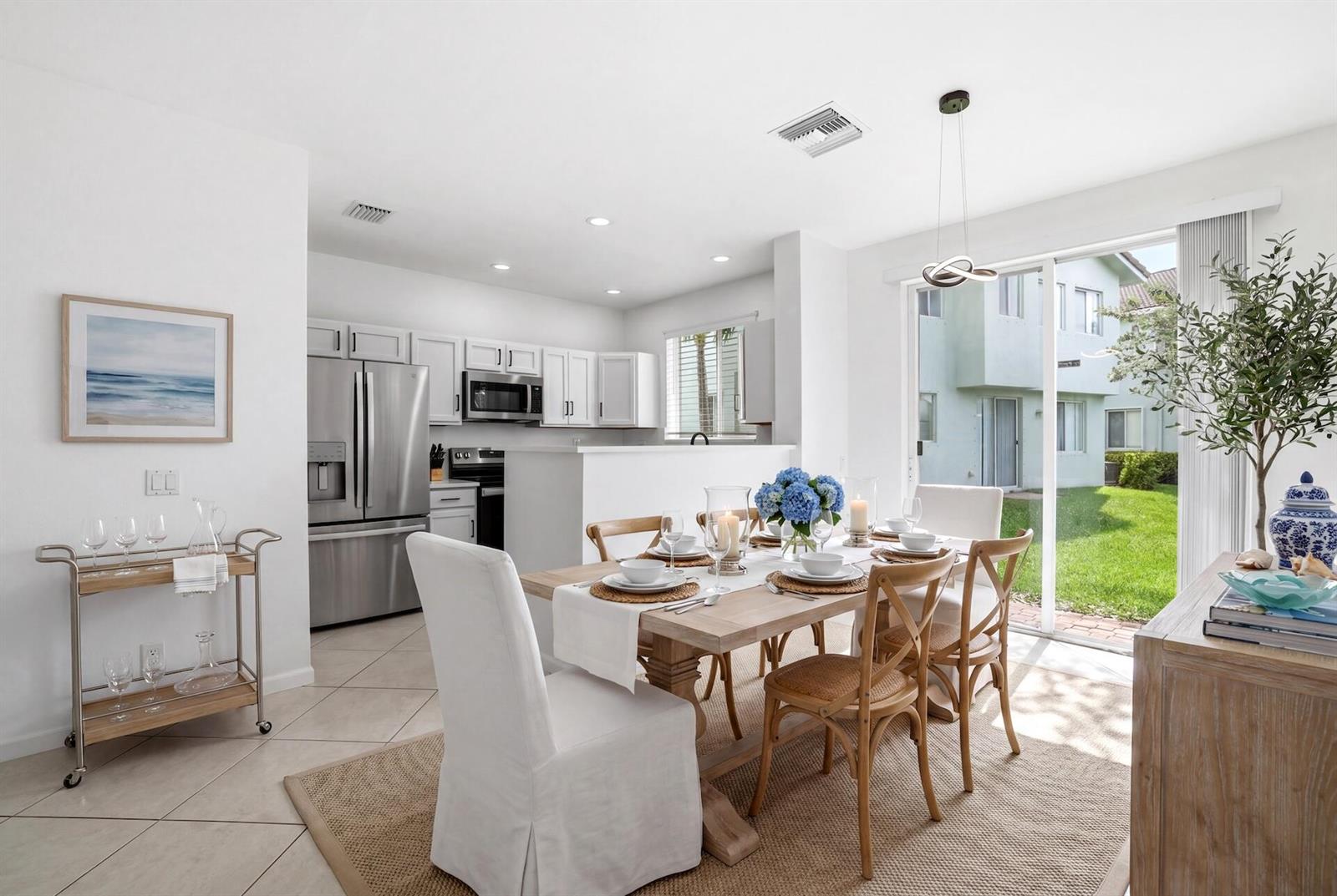 A dining area with a wooden table and chairs sits next to a kitchen with stainless appliances — 3068 Laurel Ridge Circle, Riviera Beach FL 33404, RIVIERA BEACH, FL