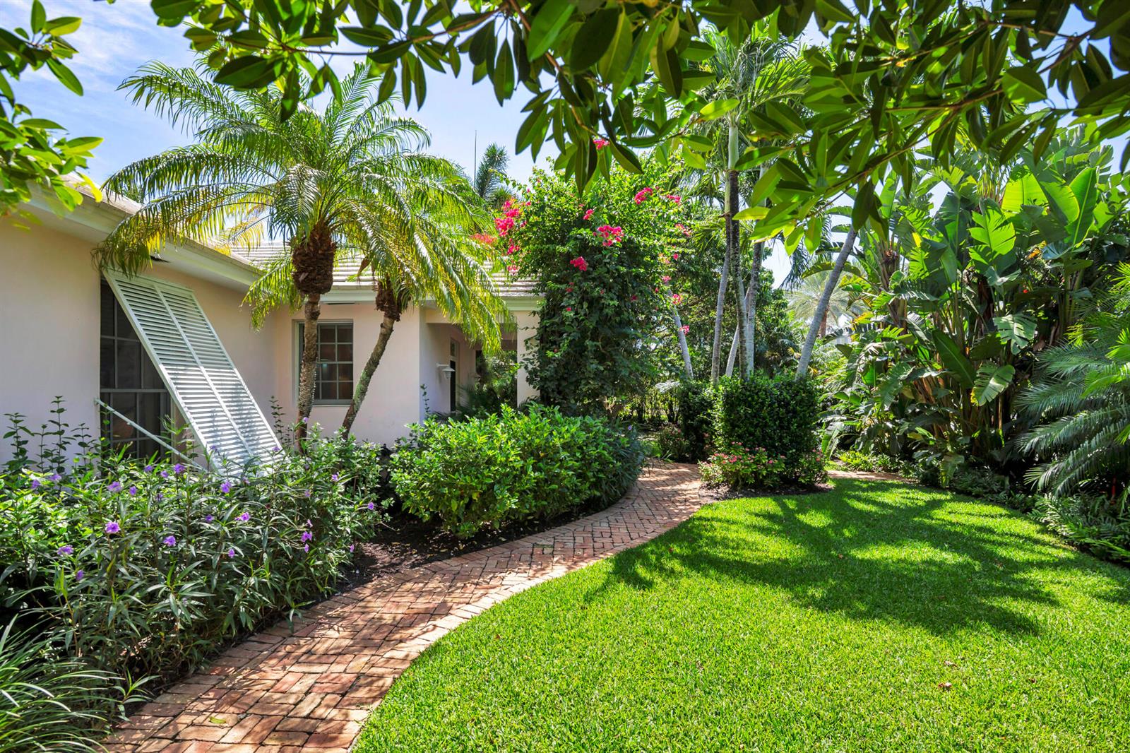 A brick walkway leads to a light-colored house surrounded by lush tropical landscaping and palms — 243 Garden Road, Palm Beach FL 33480, PALM BEACH, FL