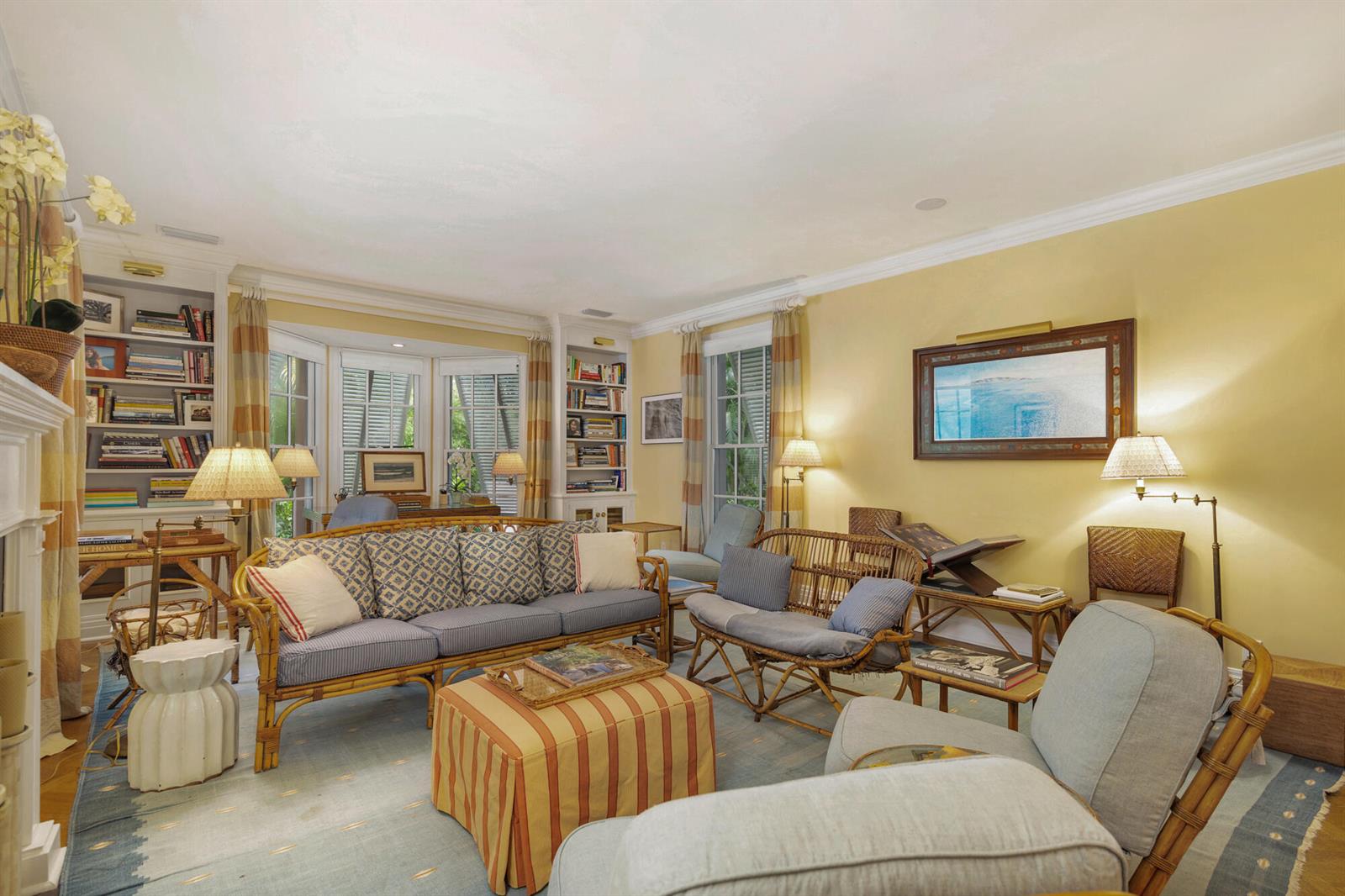 A living room features yellow walls, rattan furniture, a striped ottoman, and built-in bookshelves — 243 Garden Road, Palm Beach FL 33480, PALM BEACH, FL