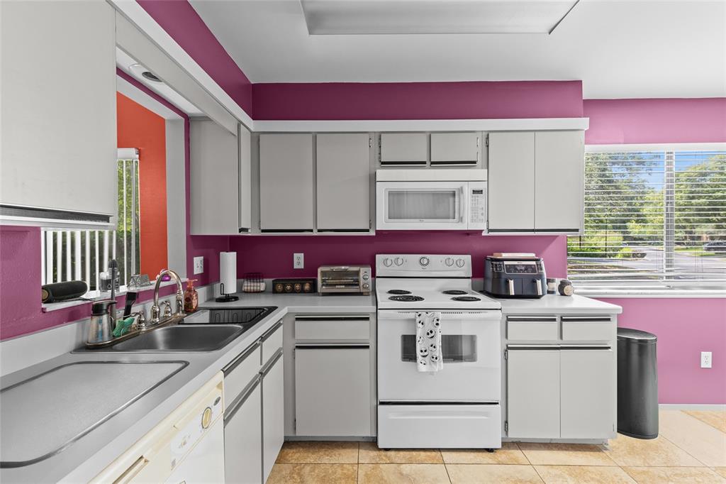 A kitchen features gray cabinets, white appliances, a double sink, and bright purple walls — 601 ALBANY COURT, LONGWOOD, FL