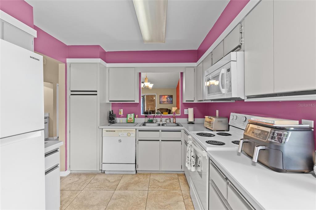 A kitchen features light gray cabinets, white appliances, pink walls, and beige tile flooring — 601 ALBANY COURT, LONGWOOD, FL