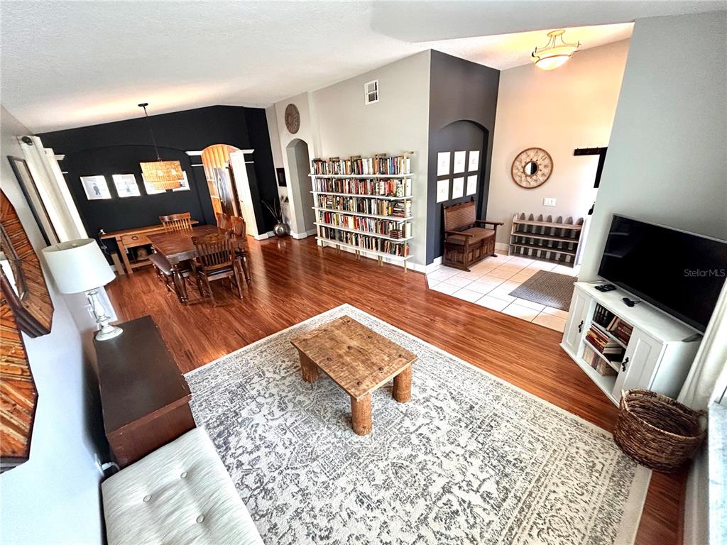 A living room with hardwood floors, a large bookshelf, and an adjacent dining area — 1737 SETTING SUN LOOP, CASSELBERRY, FL