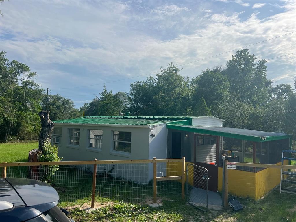 A single-story house with a green metal roof and a screened-in porch behind a fence — 20456 SE 140TH STREET, UMATILLA, FL