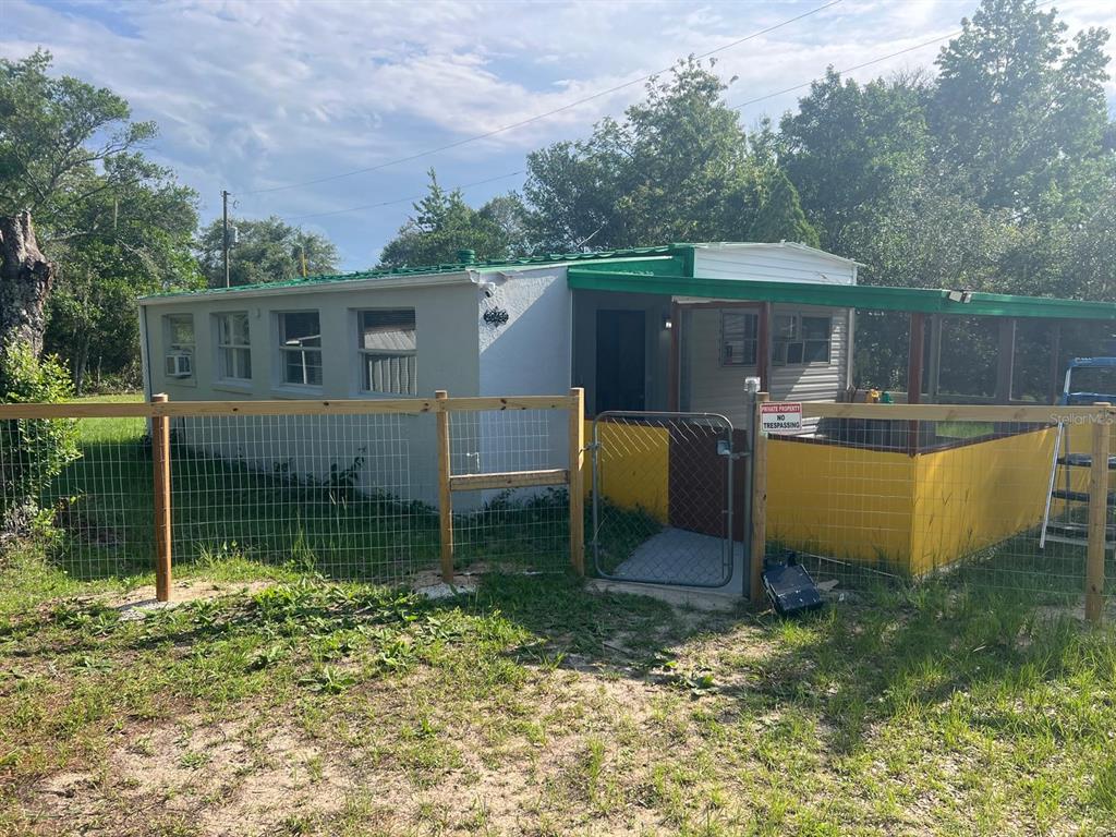 A small, single-story house with a green roof and a yellow-fenced porch behind a wire fence — 20456 SE 140TH STREET, UMATILLA, FL