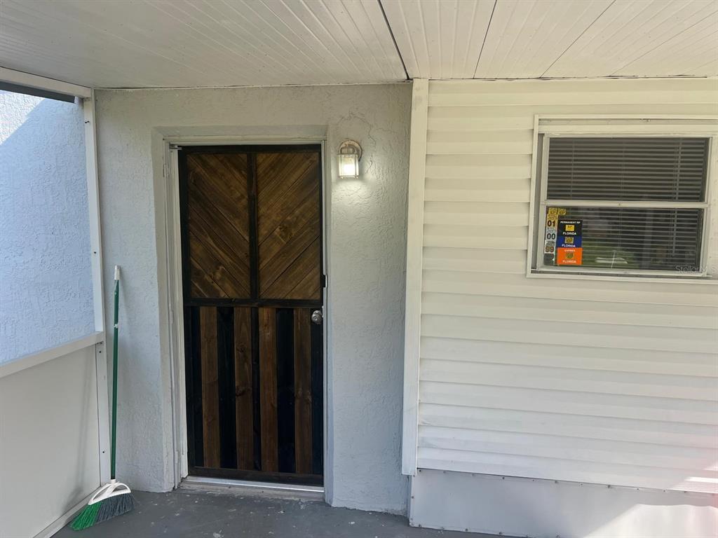 A covered porch features a wooden screen door, a wall-mounted light, and a broom — 20456 SE 140TH STREET, UMATILLA, FL