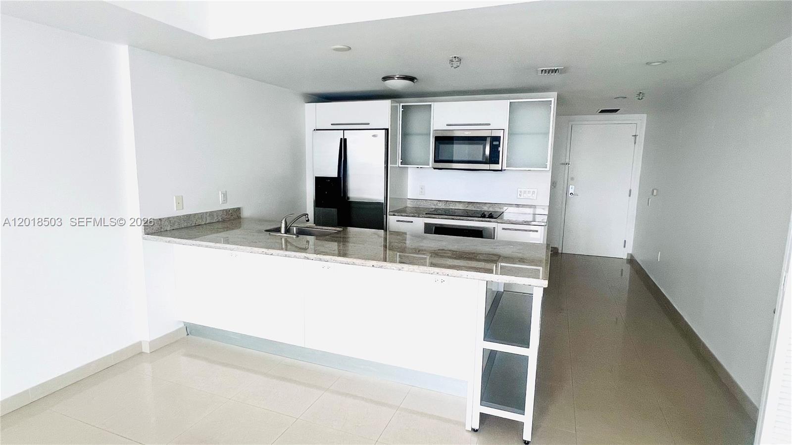 A modern kitchen features white cabinetry, granite countertops, and stainless steel appliances — 185 SW 7th St # 2805, Miami FL 33130, MIAMI, FL