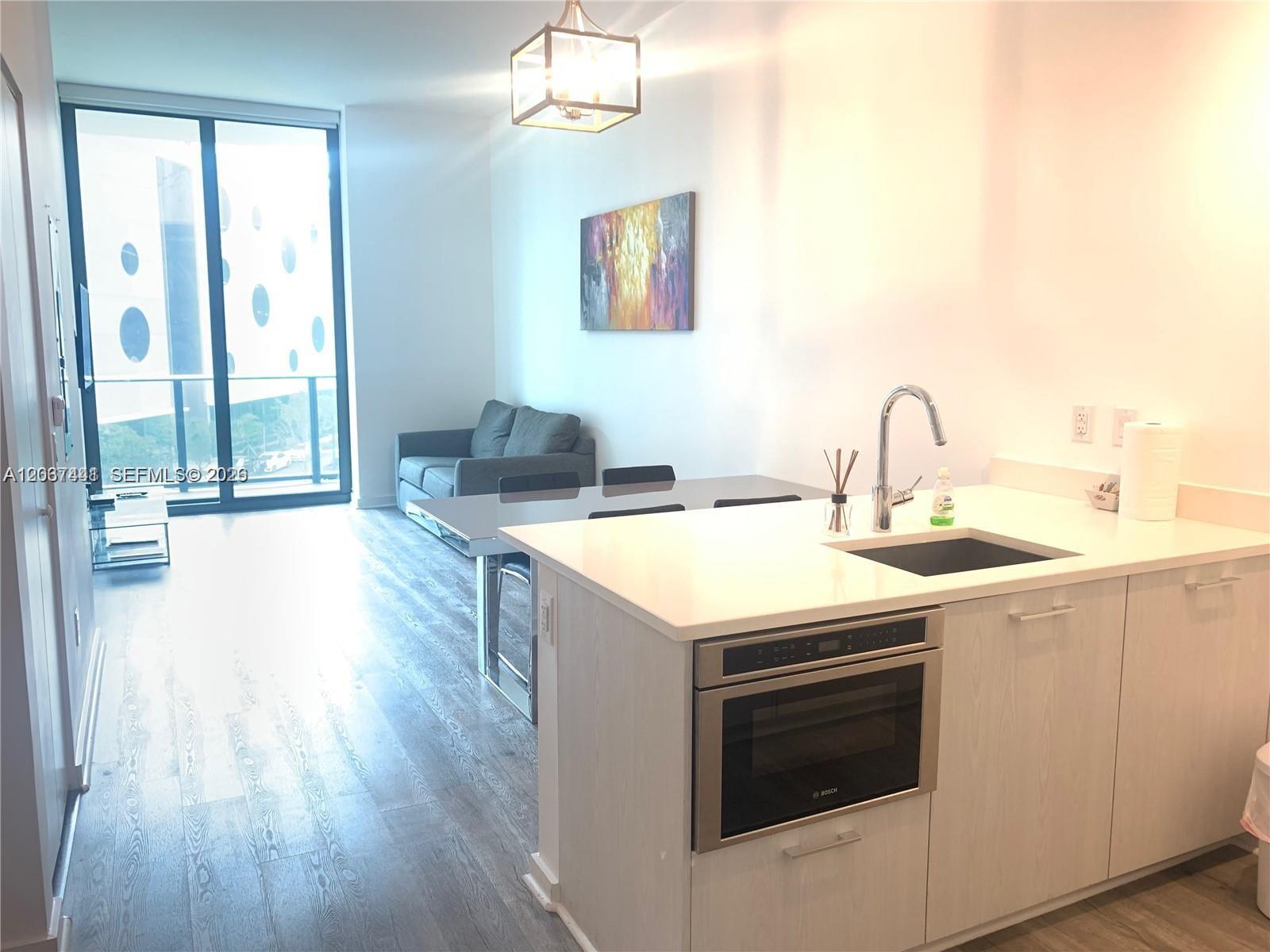 A modern kitchen island with a built-in microwave faces a dining area and living room — 501 NE 31st St # 202, Miami FL 33137, MIAMI, FL