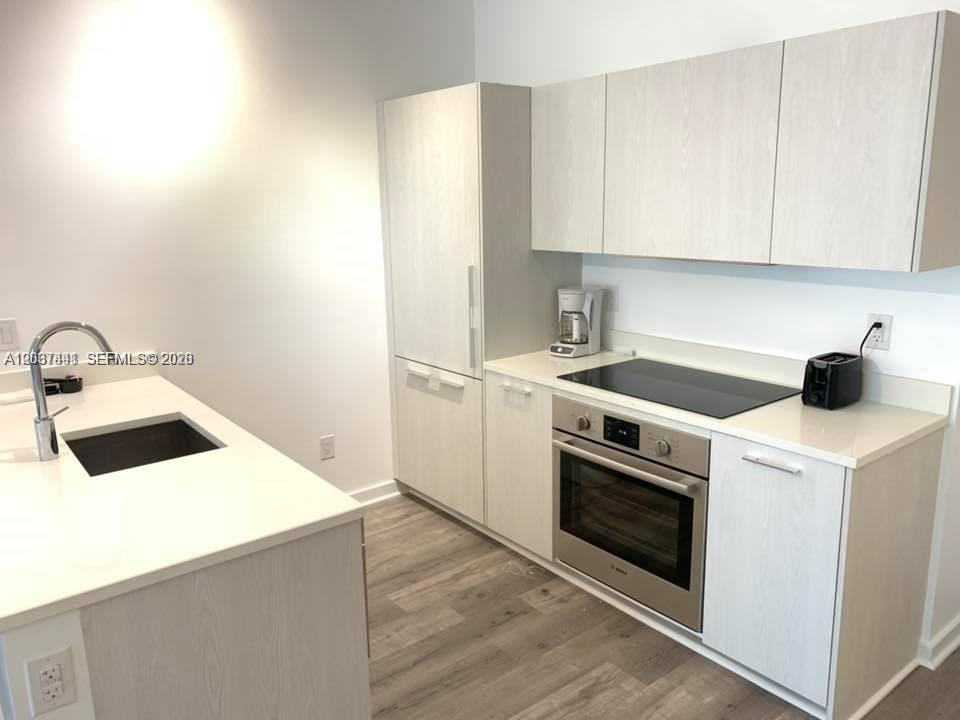 A modern kitchen features light wood cabinetry, white countertops, and stainless steel appliances — 501 NE 31st St # 202, Miami FL 33137, MIAMI, FL