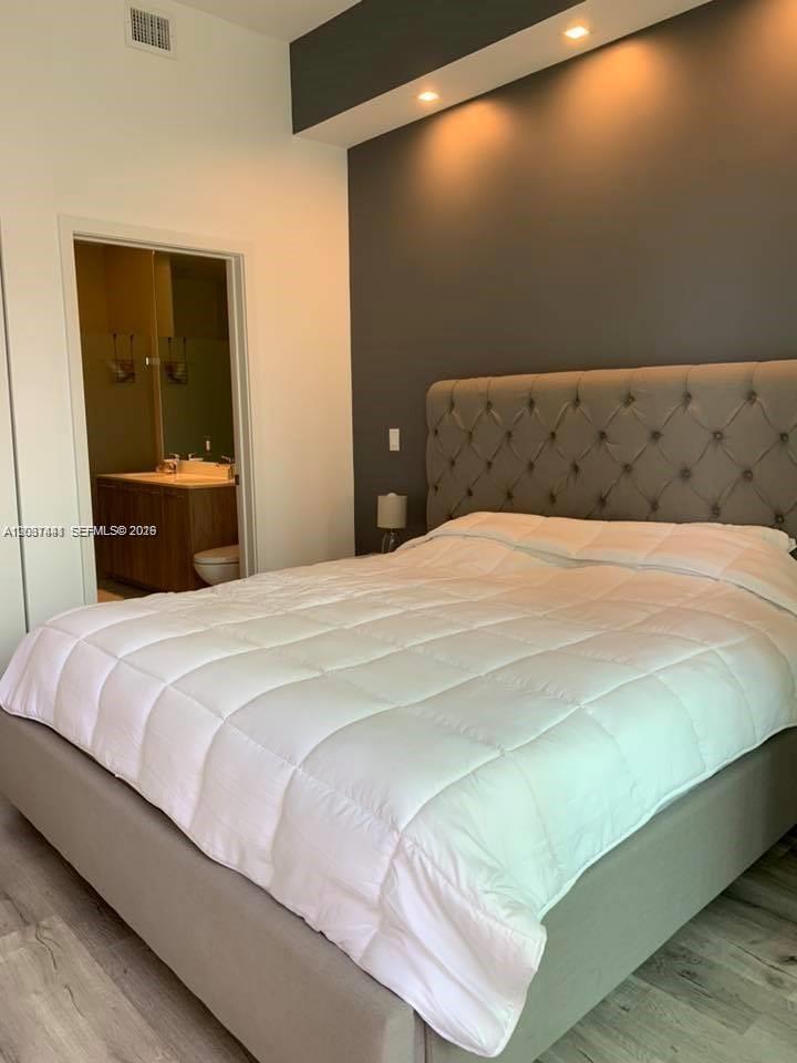 A bedroom features a tufted gray headboard, white bedding, and an adjacent bathroom — 501 NE 31st St # 202, Miami FL 33137, MIAMI, FL