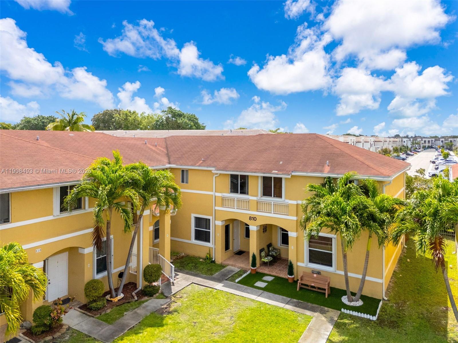 An exterior view of a two-story yellow apartment building with palm trees and landscaping — 810 NE 212th Ter # 2, Miami FL 33179, MIAMI, FL
