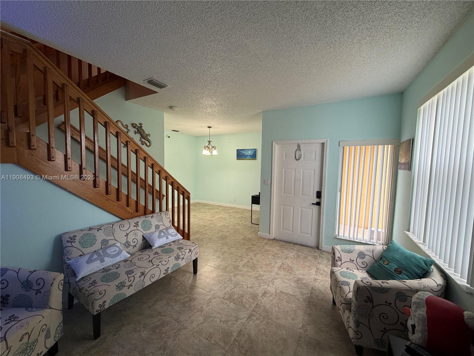 A living area features tile flooring, a wooden staircase, and light blue walls — 810 NE 212th Ter # 2, Miami FL 33179, MIAMI, FL