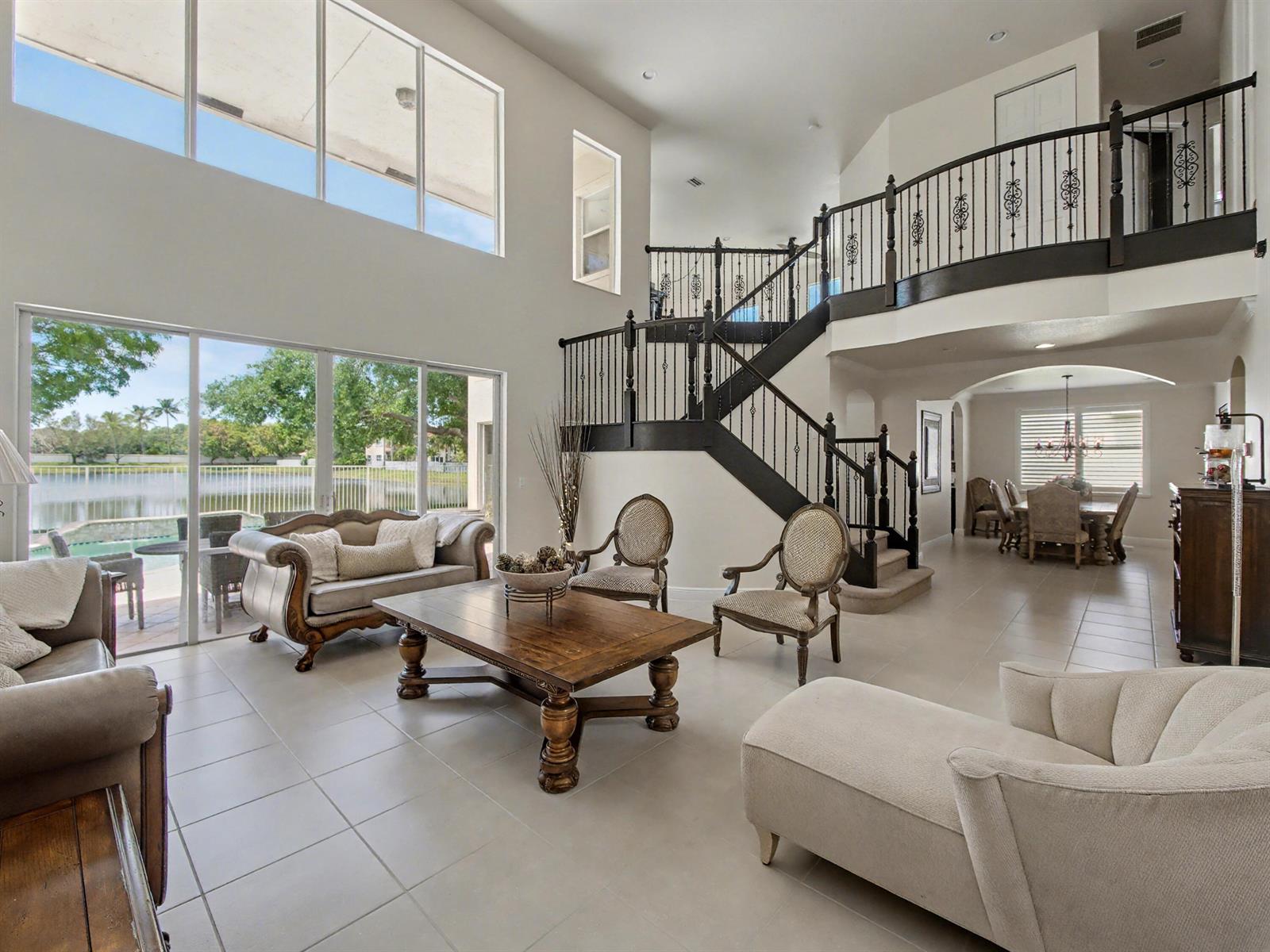 A spacious living room with a grand staircase, tile floors, and large windows overlooking water — 7244 Vía Abruzzi, Lake Worth FL 33467, LAKE WORTH, FL