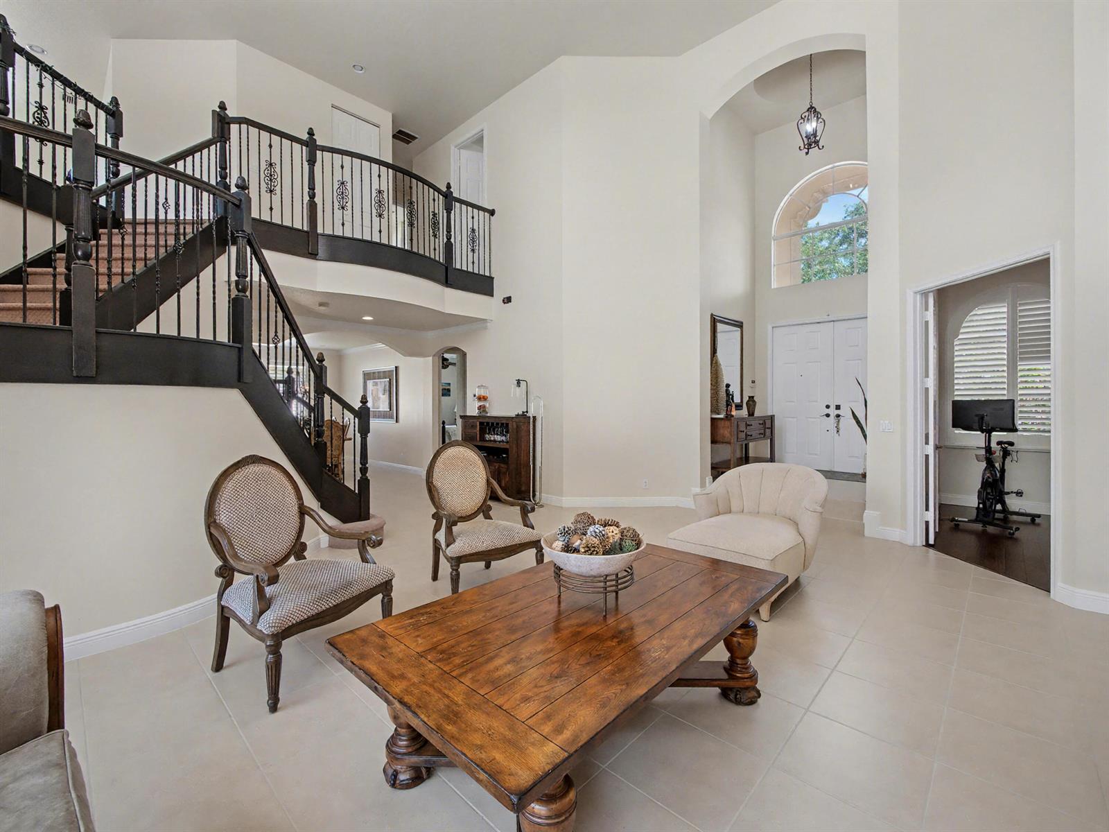 A spacious foyer features a curved staircase, tile flooring, and a large wooden coffee table — 7244 Vía Abruzzi, Lake Worth FL 33467, LAKE WORTH, FL