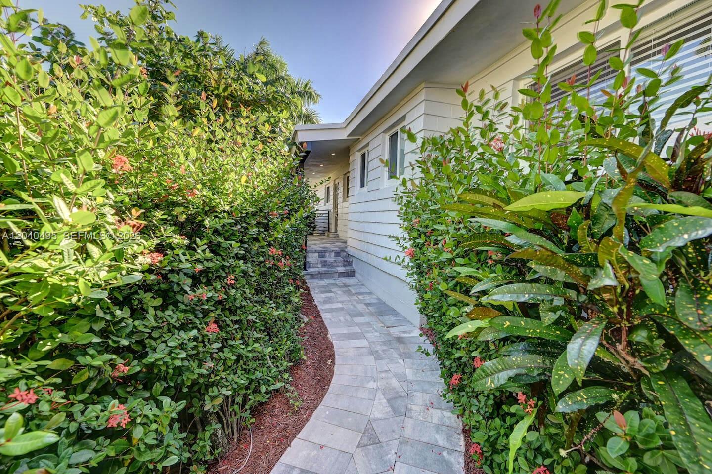A paved walkway leads between lush green hedges toward the side entrance of a house — HOLLYWOOD, FL
