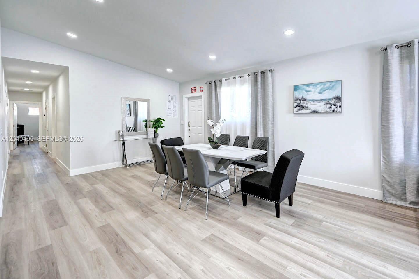 A dining room features a white table with six chairs, light wood flooring, and neutral walls — HOLLYWOOD, FL