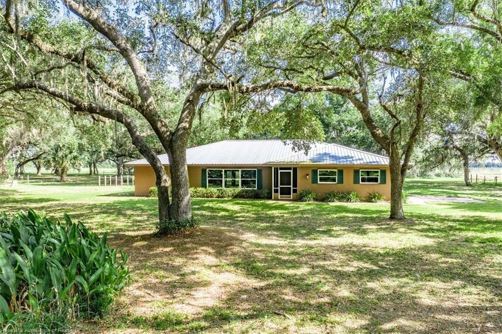 A single-story house with a metal roof sits on a grassy lot under large trees — 203 BOYER STREET, VENUS, FL