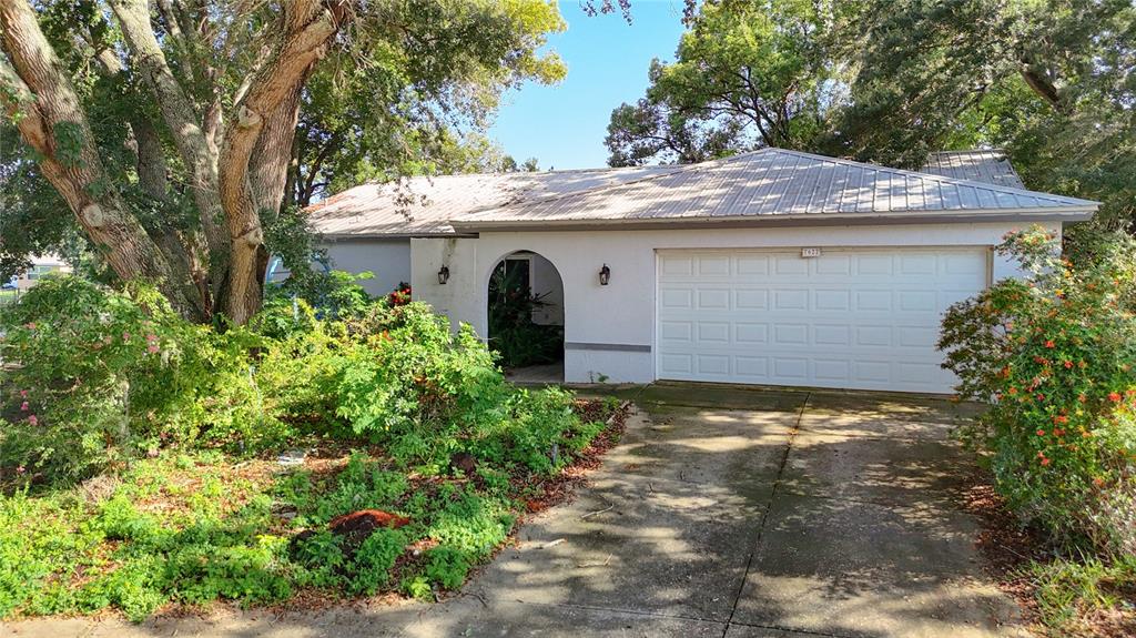 A single-story house with a white stucco exterior, metal roof, and an attached garage — 7622 CLOVIS COURT, NEW PORT RICHEY, FL