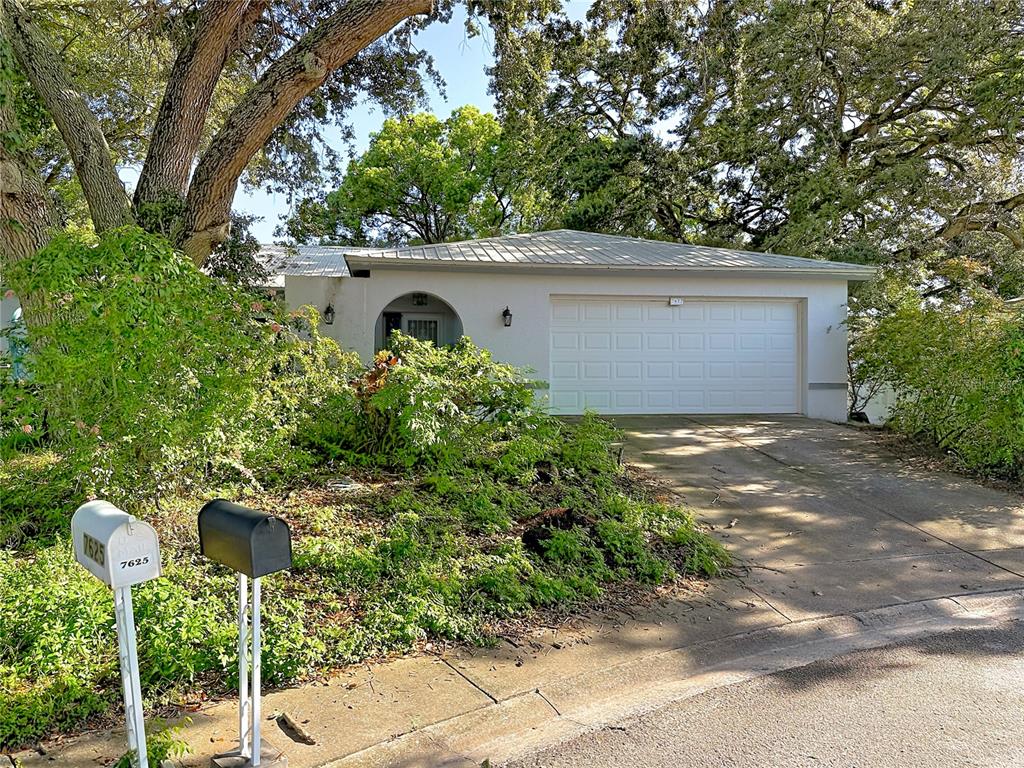 A white house with a garage and a driveway is surrounded by mature trees — 7622 CLOVIS COURT, NEW PORT RICHEY, FL