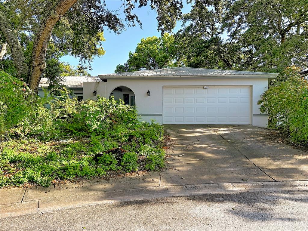 A white single-story house with a two-car garage and a large, overgrown front yard — 7622 CLOVIS COURT, NEW PORT RICHEY, FL
