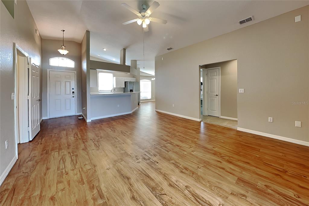 An open-concept living area features wood-look flooring, a vaulted ceiling, and an adjacent kitchen — 3382 WINCHESTER ESTATES CIRCLE, LAKELAND, FL
