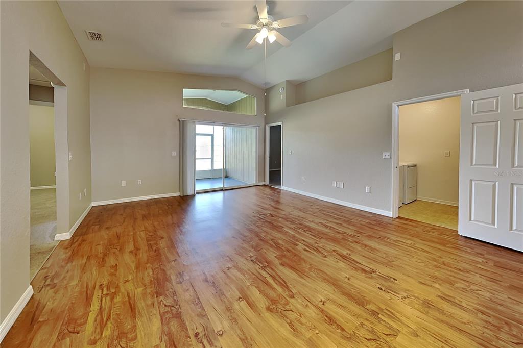 An empty living room features wood-look flooring, vaulted ceilings, a ceiling fan, and sliding glass doors — 3382 WINCHESTER ESTATES CIRCLE, LAKELAND, FL