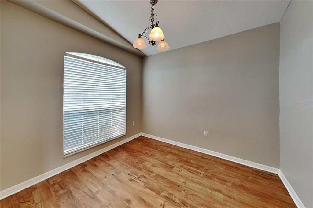 An empty room with light wood-look flooring, beige walls, a window with blinds, and a chandelier — 3382 WINCHESTER ESTATES CIRCLE, LAKELAND, FL