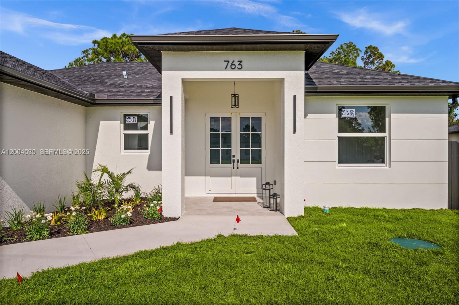 The exterior of a modern white house features a covered entryway with double glass doors — 763 Andover Ave S, Lehigh Acres FL 33974, LEHIGH ACRES, FL
